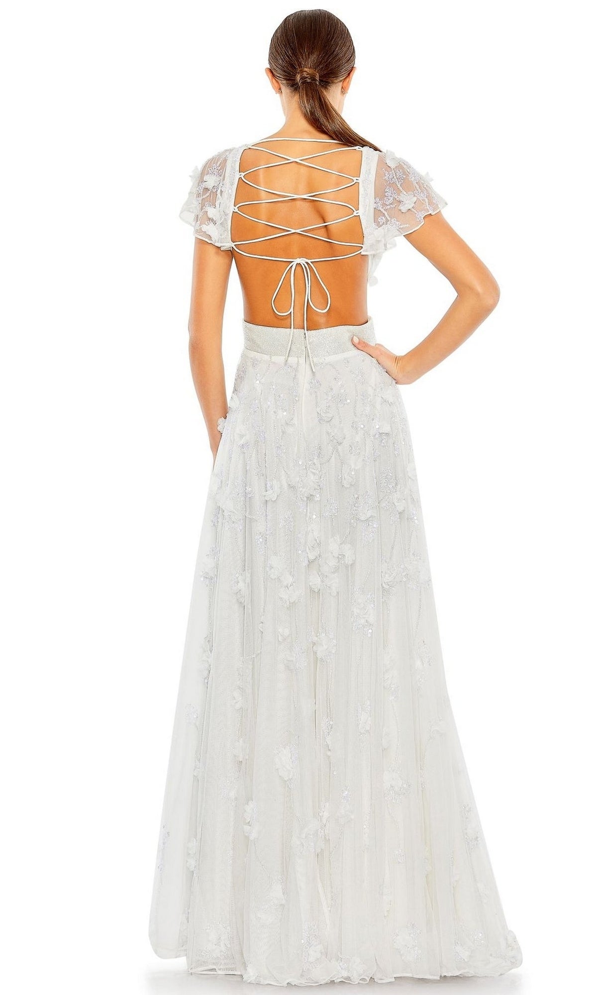 A woman with a low ponytail stands facing away, wearing the Mac Duggal Long Formal Dress 70275—an embellished, floral-detailed A-line gown featuring a lace-up open back.